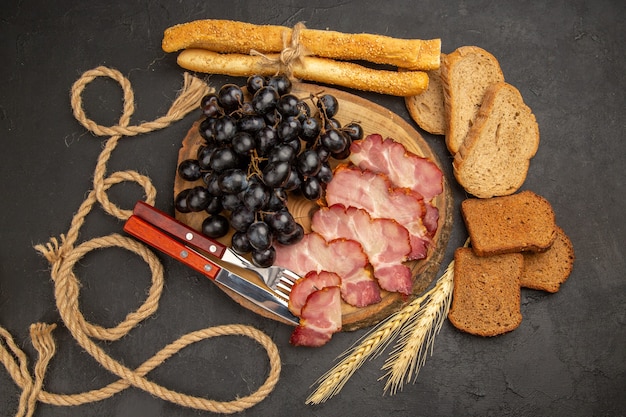 Free photo top view ham slices with grapes and bread slices on dark background