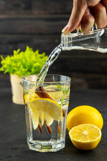 Top view of hand adding liquid glass of water with lemon and cinnamon limes on black background with free space