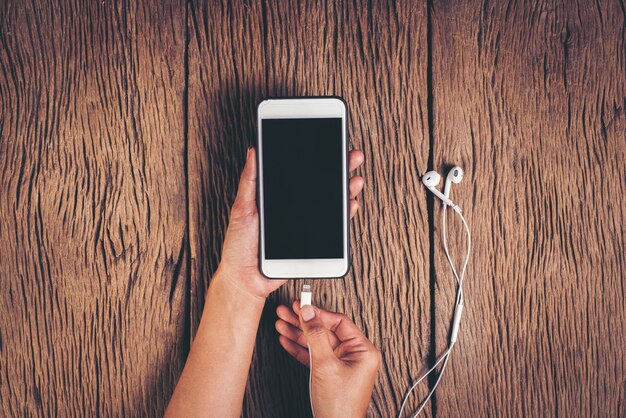 Top view hand charging phone on wood background