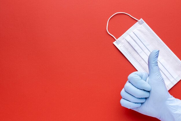 Top view of hand giving thumbs up with medical mask and copy space