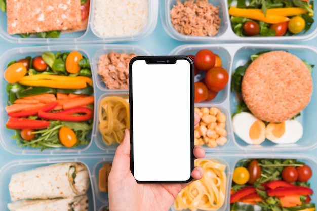 Top view hand holding blank phone over variety of lunchboxes