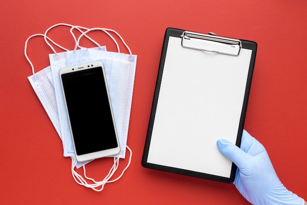 Free photo top view of hand holding clipboard with medical masks and smartphone