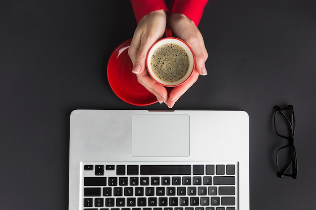 Free photo top view of hand holding cup of coffee on desk with laptop