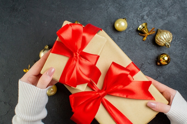 Top view of hand holding one of gift boxes with red ribbon and decoration accessories on dark background