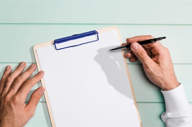 Top view hand holding a pen above copy space clipboard