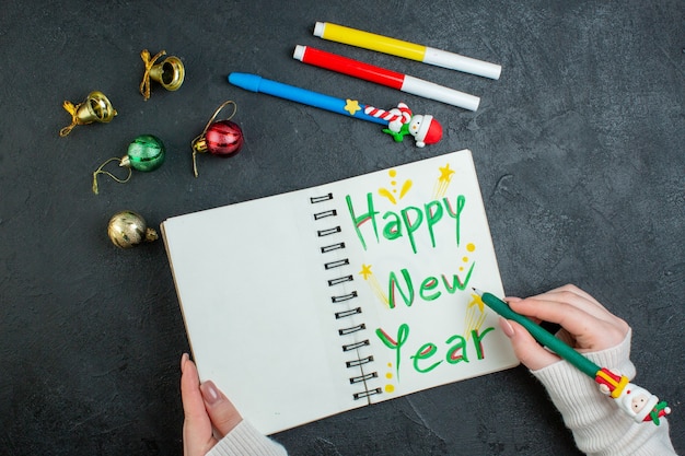 Free Photo top view of hand holding a pen on spiral notebook with happy new year writing decoration accessories on black background