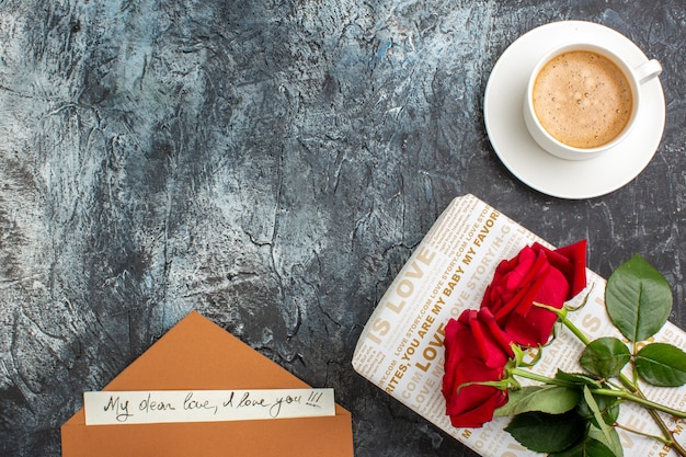 Free photo top view of hand holding red roses on beautiful gift box and cup of coffee envelope with love letter on the left side on icy dark background