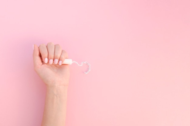 Top view hand holding tampon on pink background