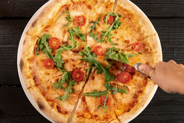 Top view of hand using pizza cutter on delicious pizza