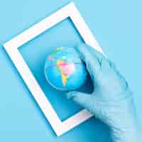 Free photo top view of hand with surgical glove holding earth globe in frame