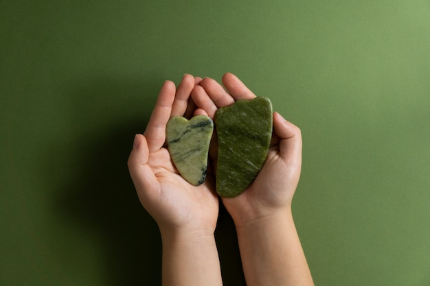 Free photo top view hands holding green gua sha