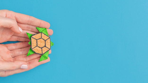 Top view of hands holding paper turtle with copy space for animal day