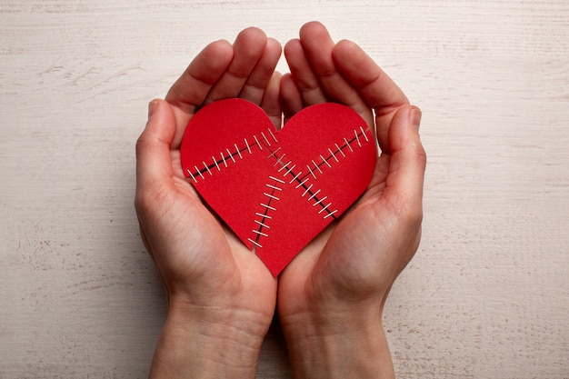 Free photo top view hands holding stapled broken heart