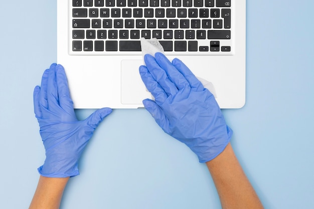 Free photo top view of hands with surgical gloves disinfecting laptop