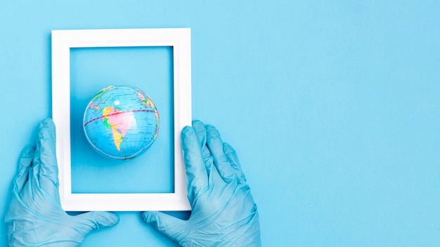 Free photo top view of hands with surgical gloves holding frame over earth globe with copy space