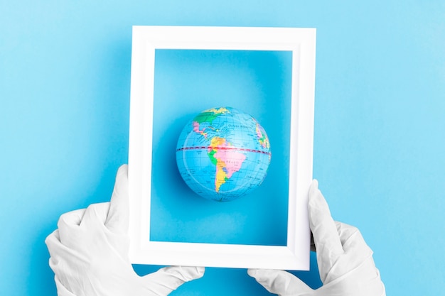 Top view of hands with surgical gloves holding frame over earth globe