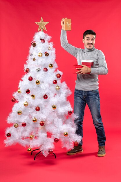 Top view of handsome adult in a gray blouse standing near the decorated white Christmas tree