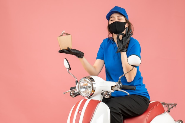 Free Photo top view of happy delivery person wearing medical mask and gloves sitting on scooter delivering orders on pastel peach background