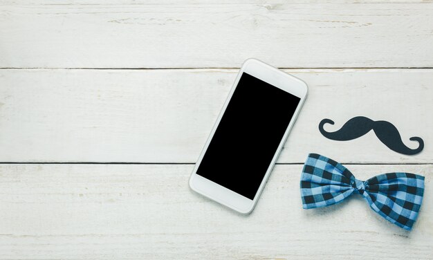 Top view Happy Father day.White mobile phone on rustic wooden background.Sign father is mustache and vintage bow tie.