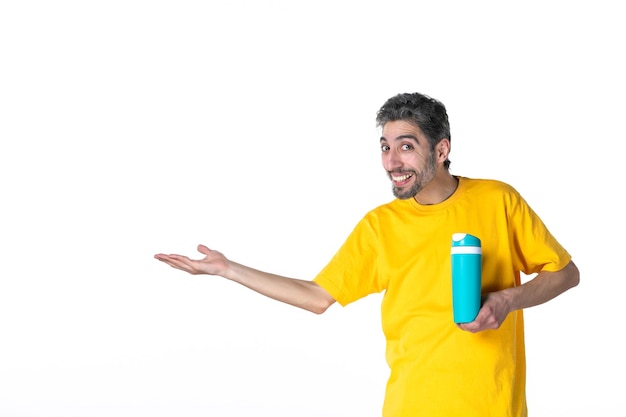 Top view of happy young male in yellow shirt and showing blue thermos pointing something on the right side on white background