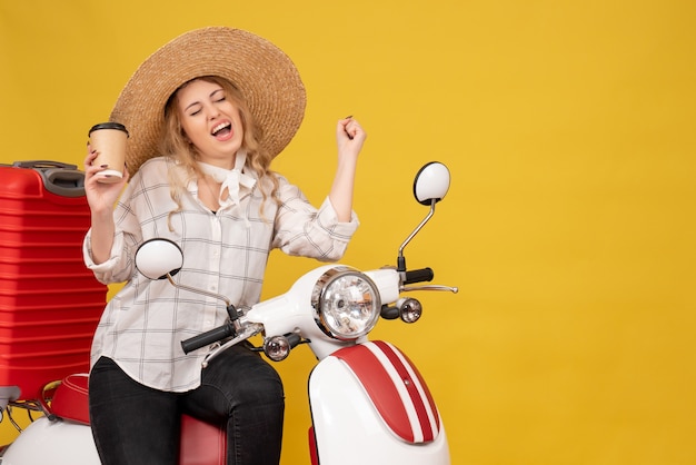 Top view of happy young woman wearing hat and sitting on motorcycle and holding coffee enjoying her succeess