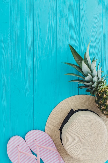 Top view of hat, pineapple and flip flops on blue wooden surface