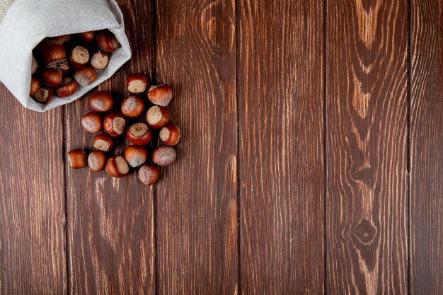 Top view of hazelnuts in shell scattered from a sack on wooden background with copy space