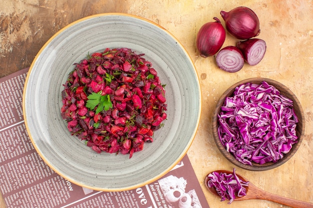 Top view healthy beet salad on a gray plate with red onions and chopped cabbage in a bowl on a wooden table