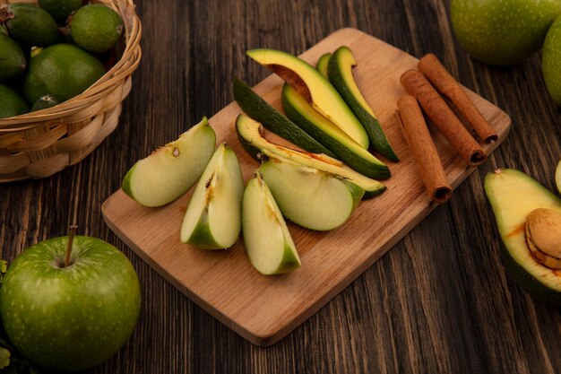 Top view of healthy chopped slices of avocados on a wooden kitchen board with cinnamon sticks and slices of apple with feijoas on a wooden surface