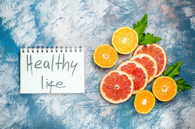 Top view healthy life written on notepad cut oranges and grapefruits on blue white surface