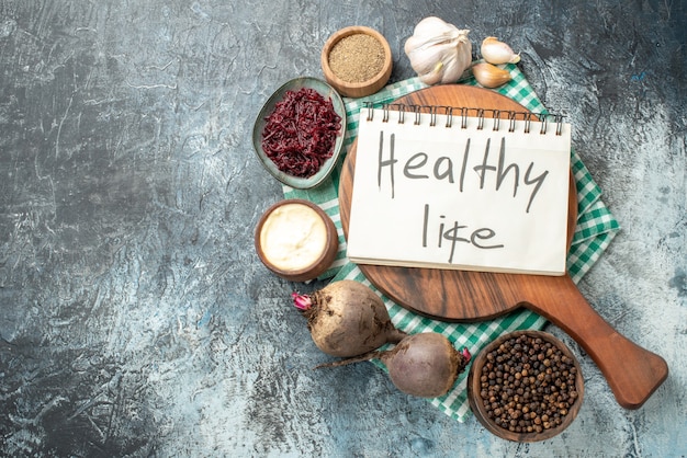 Free Photo top view healthy life written on notepad on wood board spices in bowls garlic beets on grey table