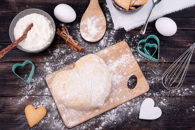 Top view of heart-shaped dough with kitchen utensils