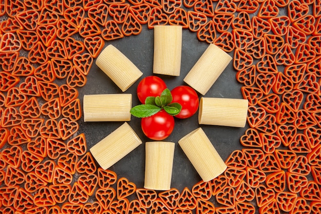 Free photo top view heart shaped italian pasta rigatoni and cherry tomatoes on dark table