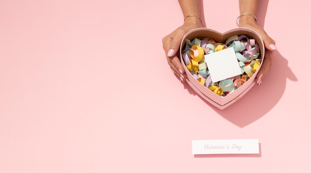 Top view of heart-shaped tin box with confetti for valentines day and woman's hands