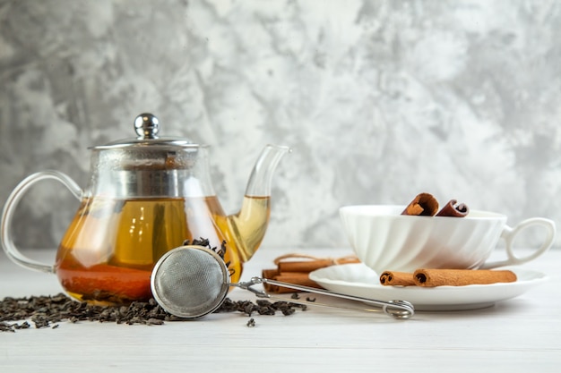 Free photo top view of herbal tea in a glass pot and in a cup with cinnamon limes on white background