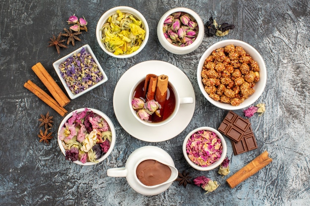 Top view of herbal tea with dry flowers and chocolate and nuts on grey ground