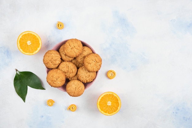 Top view of homemade cookies with half cut orange over white table.