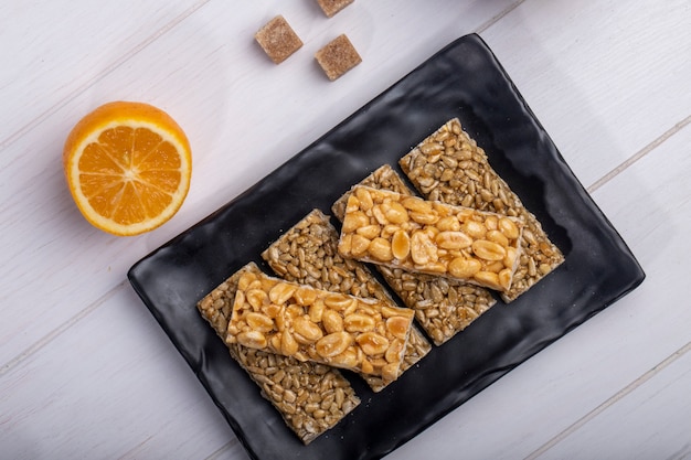 Top view of honey bars with peanuts and sunflower seeds on a black platter with orange on rustic