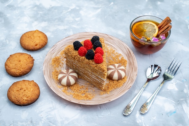 A top view honey cake slice inside plate with candies cookies and tea on the blue background cookie tea cake 