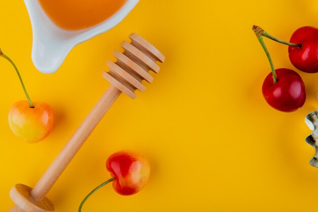 Top view of honey with wood spoon and fresh ripe rainier cherries on yellow