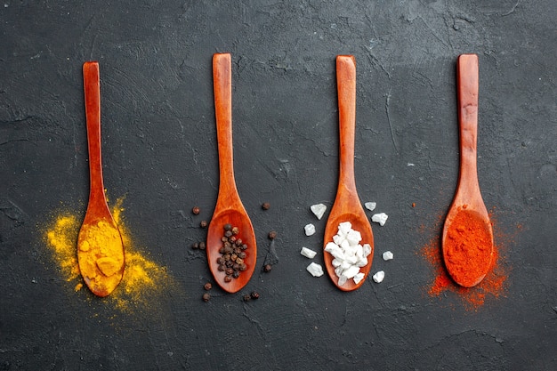 Free Photo top view horizontal row wooden spoons with turmeric black pepper sae salt red pepper powder on black table