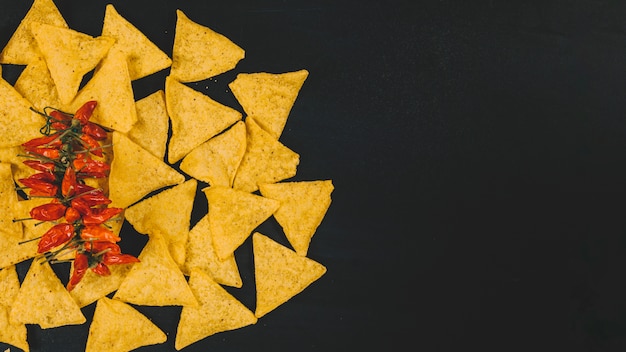 Free Photo top view of hot mexican nachos chips with red chilies over black backdrop