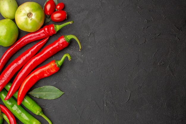 Top view hot red and green peppers and tomatoes bay leaves at the left side of black ground with free space