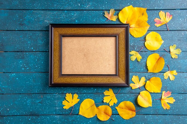 Top view of inside empty wooden picture frame and yellow leaves in various size on blue background