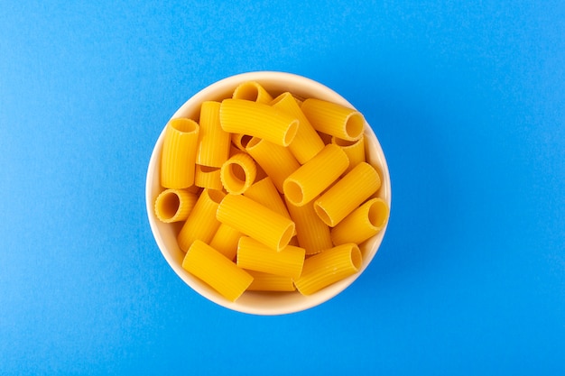 Free photo a top view italia dry pasta formed little yellow raw pasta inside cream colored round bowl isolated on the blue background italian spaghetti food pasta