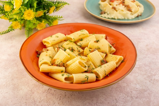 A top view italian pasta cooked tasty with dried greens and salted inside round orange plate with flower on pink desk