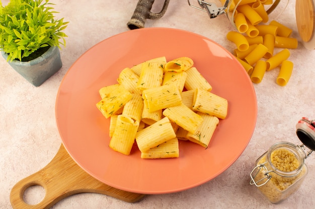 A top view italian pasta tasty meal inside pink plate along with flower and raw pasta on pink