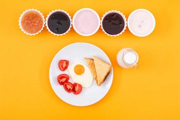 Top view of jam with yogurt and fried egg on yellow surface horizontal