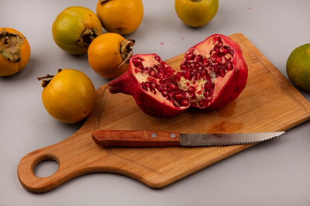 Free photo top view of juicy halved pomegranate on a wooden kitchen board with knife with persimmon fruits isolated