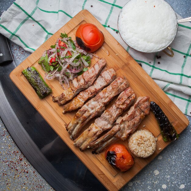 Top view kebab ribs with fried vegetables and chopped onion and ayran and knife in cutting board